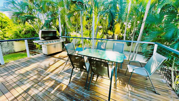 Terraza al aire libre con una parrilla, mesa y sillas, rodeada de exuberante vegetación.