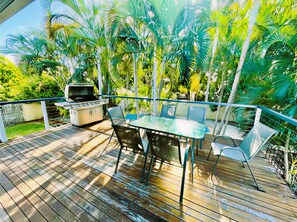 An outdoor deck with a grill, table, and chairs, surrounded by lush greenery. - Relax & Unwind: 5BR Home with Pool Near CBD (Vincent)