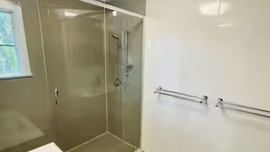 Un baño moderno con cabina de ducha de vidrio, un lavabo blanco y una alfombra de baño azul.