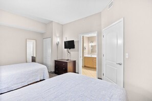 Ein Hotelzimmer mit zwei Betten, einem Fernseher, einem Schminktisch und einem durchgehenden Türspalt einsehbarer Badezimmer.