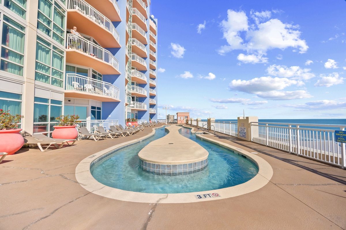 A pool area with lounge chairs and a view of the ocean.