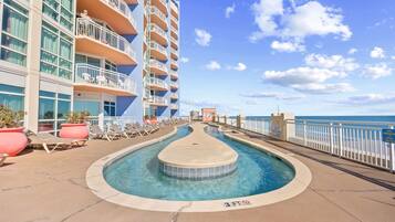 A pool area with lounge chairs and a view of the ocean.