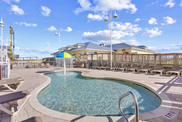 A swimming pool with a curved design, surrounded by lounge chairs and a wooden deck.