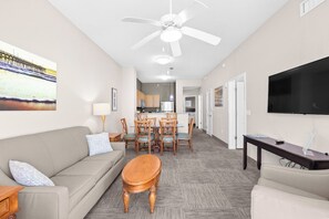 A living room with a sofa, a wooden coffee table, a TV, and a ceiling fan. - 2/2 condo at Cherry Grove Pier (North Myrtle Beach)