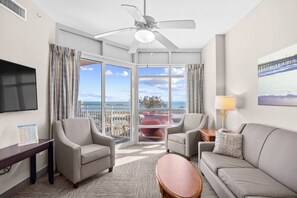 Ein Hotelzimmer mit Balkon, Deckenventilator, Flachbildfernseher und großem Fenster mit Meerblick.