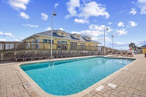 A swimming pool with lounge chairs, a wooden fence, and a building with a yellow facade in the background.