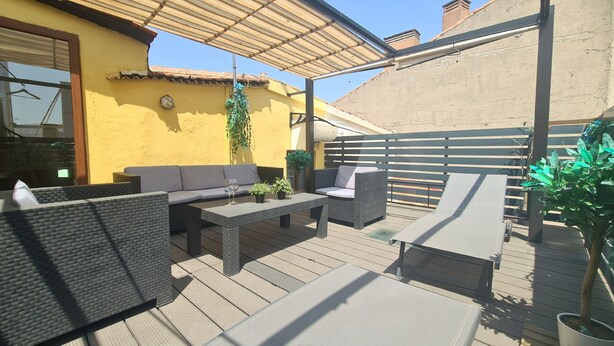 Eine Terrasse im Freien mit Korbmöbeln, einem Tisch und Blumentöpfen.