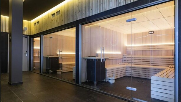 Eine moderne Sauna mit Glaswänden, Holzbänken und einer Decke mit integrierter Beleuchtung.