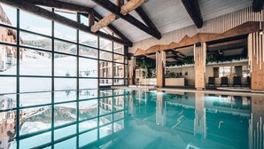 Ein überdachter Pool mit großen Fenstern und Blick auf eine gebirgige Landschaft.