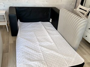 Un lit avec un matelas matelassé blanc, une tête de lit noire et un oreiller à rayures.