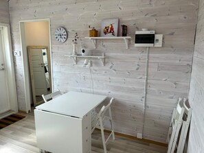 Une pièce comprenant une table blanche, des chaises, une horloge, un four à micro-ondes et une étagère sur laquelle sont disposés divers objets.