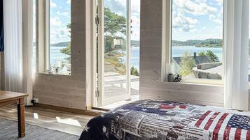 A bedroom with a large window, a bed with a patterned bedspread, and a view of a lake and hills.