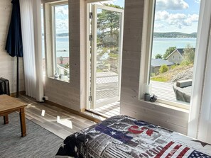 A room with a bed, a table, and a view of a lake through large windows. - 6 Person Holiday Home in Svanesund (Svanesund)