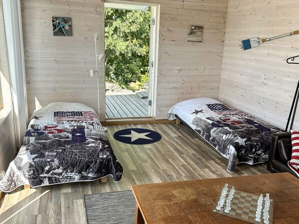 Une pièce avec deux lits, un plancher en bois, un jeu d’échecs et une porte donnant sur l’extérieur.