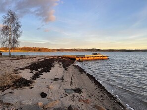 A beach with a dock extending into calm waters, surrounded by trees and a distant shoreline. - 6 Person Holiday Home in Svanesund (Svanesund)