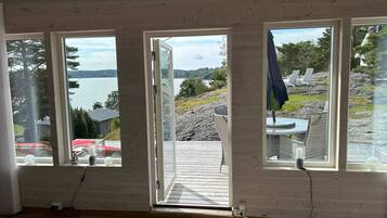 A room with a large wooden door leading to an outdoor deck with a view of a lake and rocky terrain.