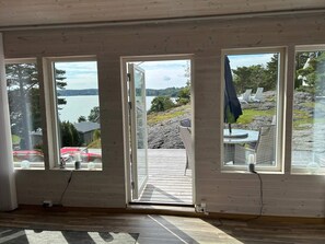 A room with a large wooden door leading to an outdoor deck with a view of a lake and rocky terrain. - 6 Person Holiday Home in Svanesund (Svanesund)