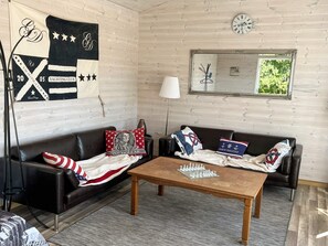 A room with a wooden wall, a chessboard on a coffee table, two sofas with American flag pillows, a lamp, and a framed mirror. - 6 Person Holiday Home in Svanesund (Svanesund)