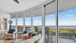 Ein geräumiger Balkon mit Blick auf den Strand, eine Couch mit gemusterten Kissen und eine Uhr auf einem Stativ.