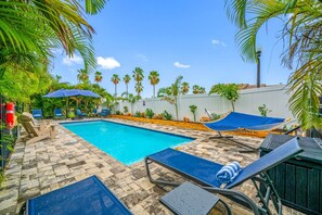 Ein Swimmingpool mit Liegestühlen und einer Hängematte, umgeben von Palmen und einer weißen Mauer.