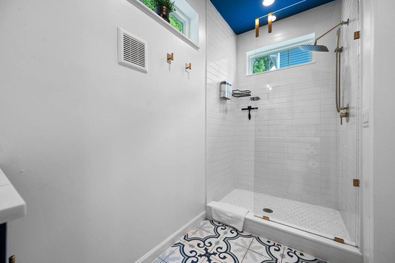 A modern shower with a glass door, a white tiled floor, and a blue ceiling.