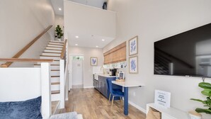 Un apartamento moderno con una escalera, una cocina con armarios azules, un comedor y un televisor grande montado en la pared.