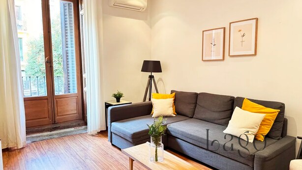 A modern living room with a grey sofa, yellow and white cushions, a small table with a vase, and a floor lamp. - Apartment two steps away from Plaza Mayor (Madrid)