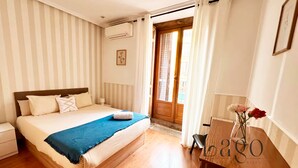 A bedroom with a bed, a nightstand, a desk with a vase, and a door leading outside. - Apartment two steps away from Plaza Mayor (Madrid)