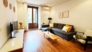 A modern living room with a sofa, a coffee table, a TV, and a door leading to an outdoor area. - Apartment two steps away from Plaza Mayor (Madrid)