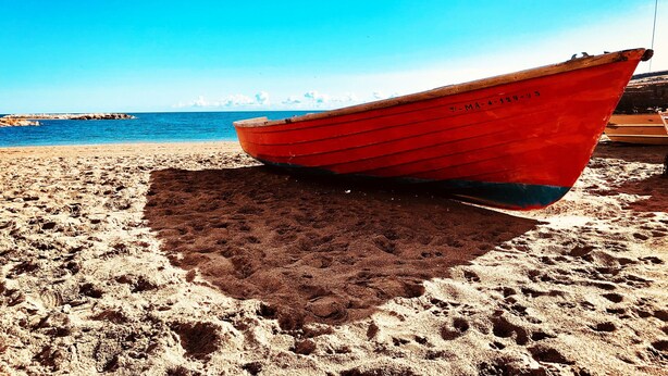 A red boat on a sandy beach with a clear blue sky and calm sea in the background. - Casa Chica (Málaga)
