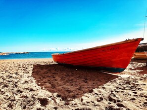 A red boat on a sandy beach with a clear blue sky and calm sea in the background. - Casa Chica (Málaga)