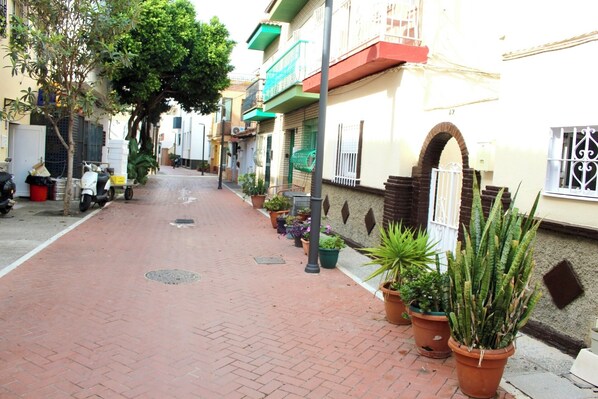 Uma rua pavimentada para pedestres, bordeada por vasos de plantas, com uma scooter estacionada na lateral.
