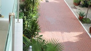 A red brick pathway lined with potted plants and umbrellas, leading to a building with a white facade and balconies. - Casa Chica (Málaga)