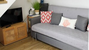 A modern living room with a grey sofa, wooden staircase, and a flat-screen TV. - Casa Chica (Málaga)