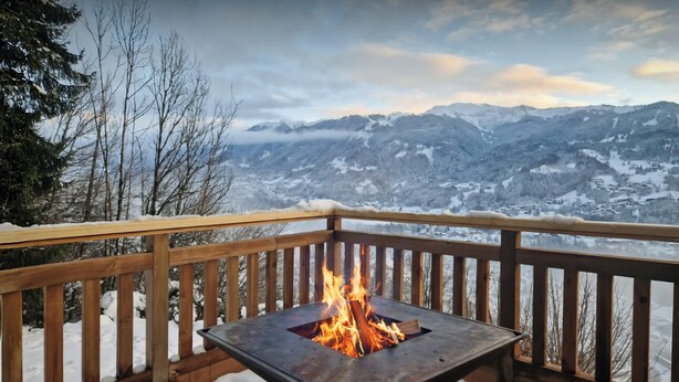 Une terrasse dotée d’un foyer métallique, entourée de neige, et offrant une vue sur un paysage montagneux.