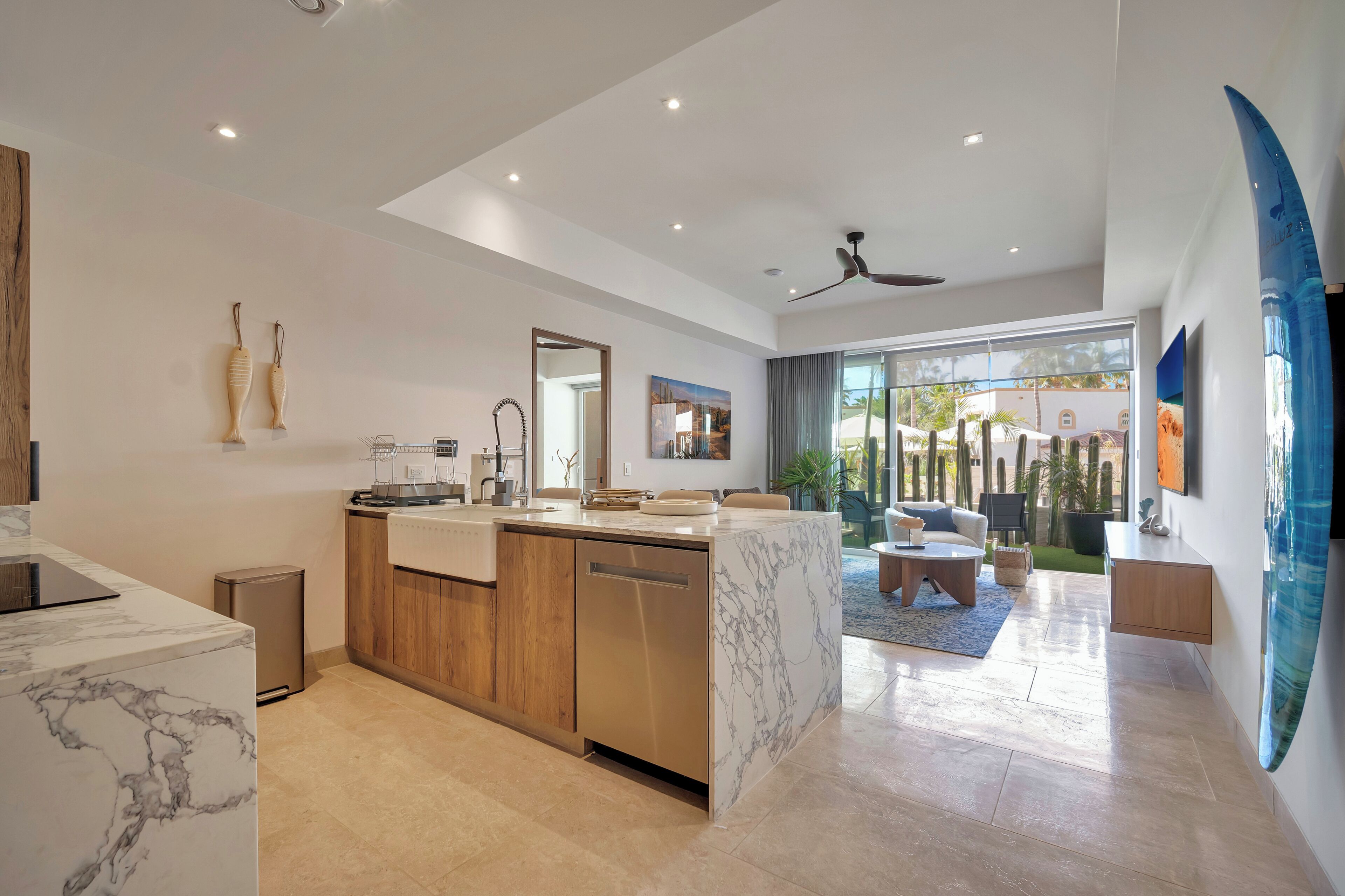Una cocina moderna con encimera de mármol, armarios de madera y lavavajillas. Hay una zona de comedor con sofá y una mesa de centro.