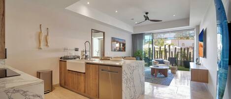 Una cocina moderna con encimera de mármol, armarios de madera y lavavajillas. Hay una zona de comedor con sofá y una mesa de centro.