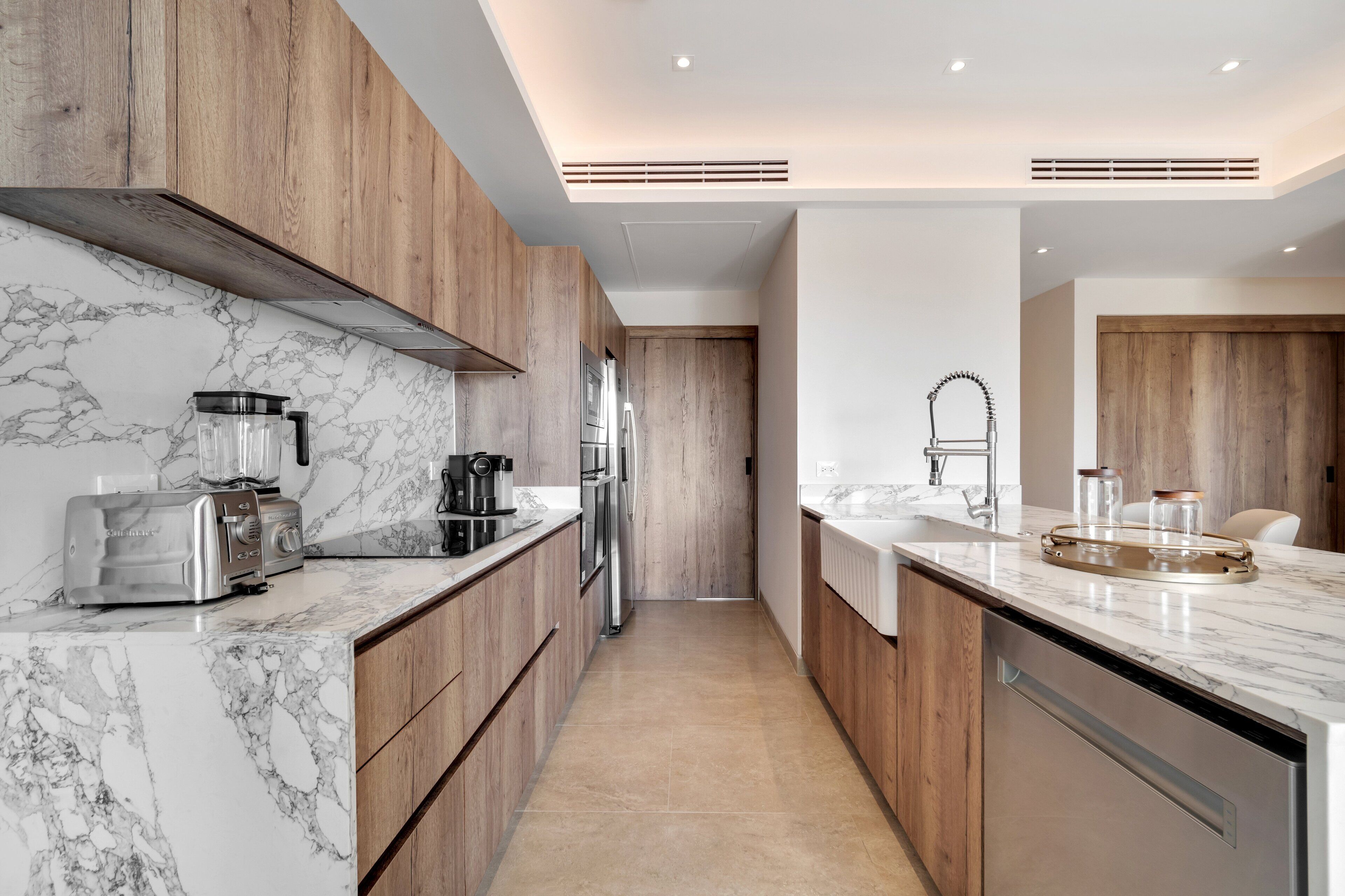 A modern kitchen with marble countertops, wooden cabinets, stainless steel appliances, and a central island with a sink.
