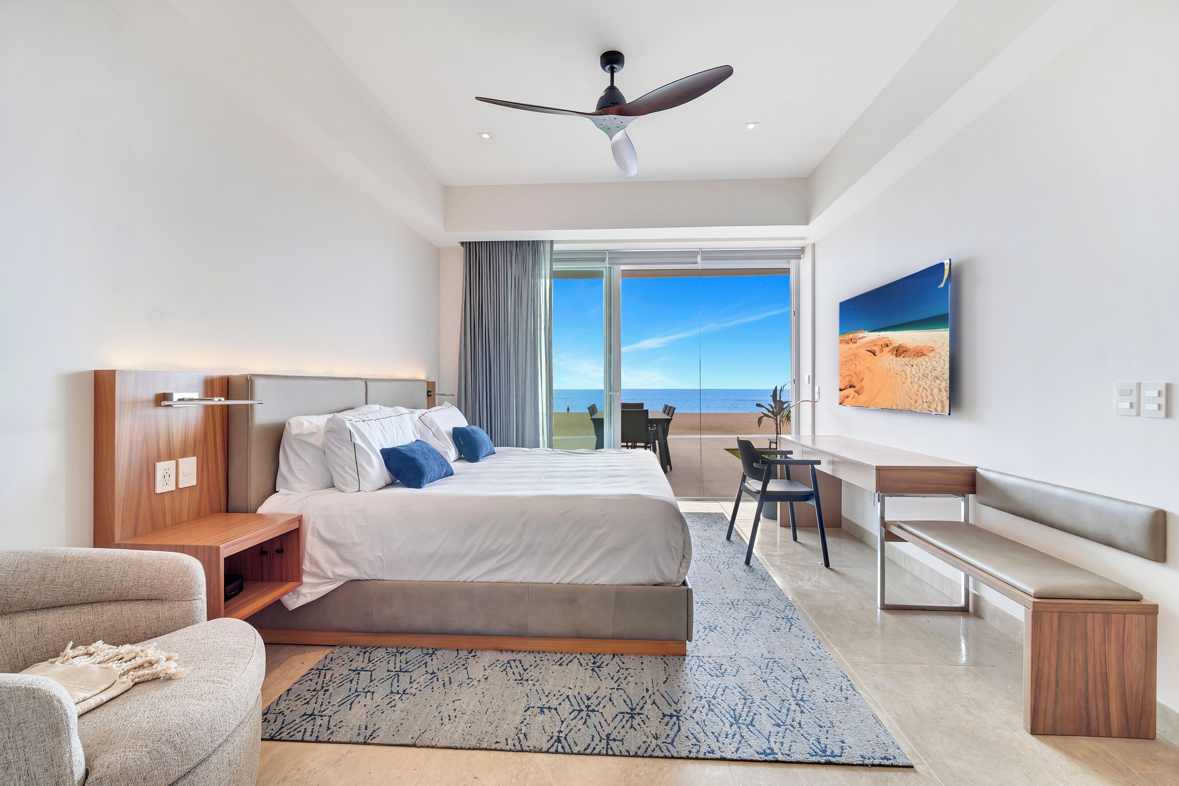 Una habitación de hotel moderna con una cama grande, un escritorio, una silla, un banco y un ventilador de techo.