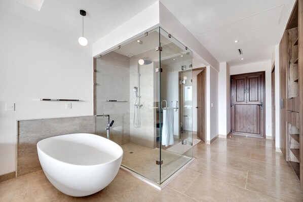 A modern bathroom with a freestanding bathtub, a glass-enclosed shower, and a wooden door.