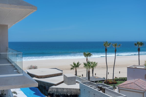 Une propriété située en bord de mer, dotée d’une piscine, d’un balcon avec des garde-corps en verre et offrant une vue sur l’océan.