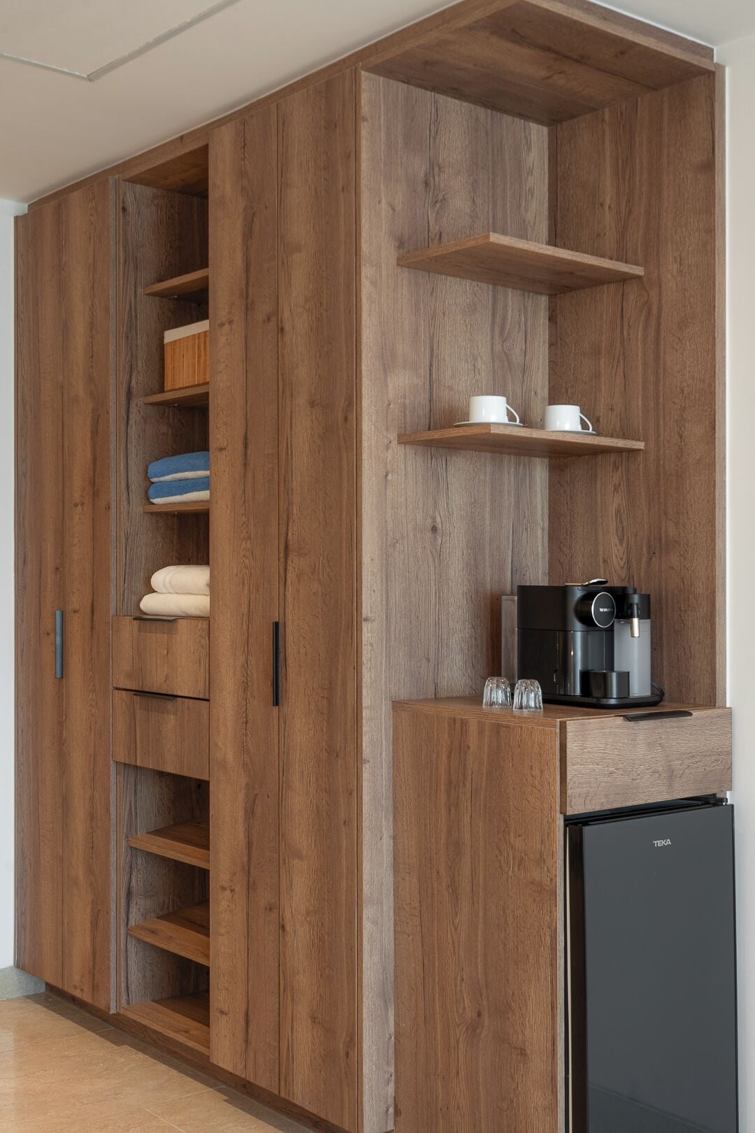 Ein Holzkleiderschrank mit mehreren Einlegeböden und Schubladen, eine Kaffeemaschine und ein Kühlschrank.