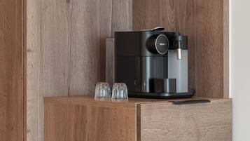 Una cocina con cafetera, dos tazas en un estante y un refrigerador.