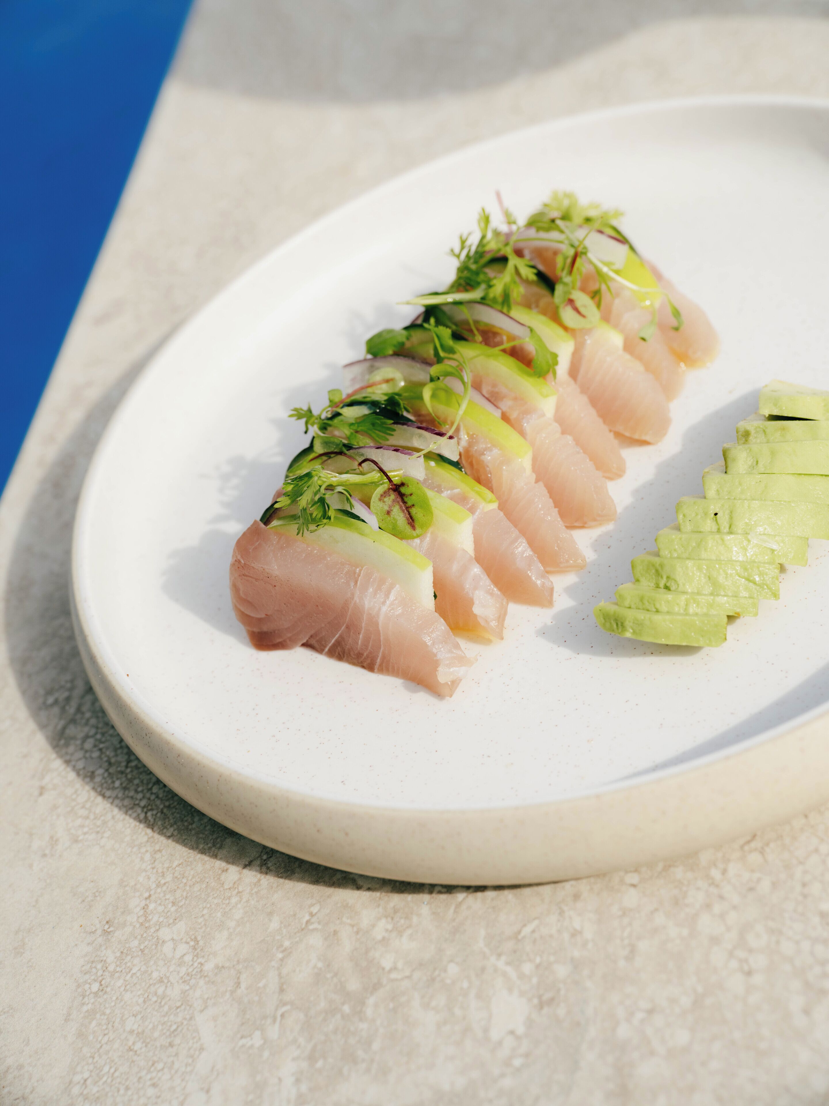 A plate with sashimi and avocado slices.