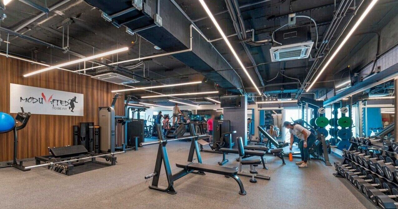 Ein Fitnessraum mit verschiedenen Trainingsgeräten, einem Schild an der Wand und Personen, die trainieren.