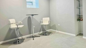 A room with two white bar stools, a small table, and a window with blinds.