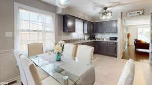 A modern kitchen with dark cabinets, a glass dining table, and a 'Welcome' sign.