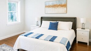 A bedroom with a bed, a ceiling fan, a window, a nightstand, a lamp, and a rug.