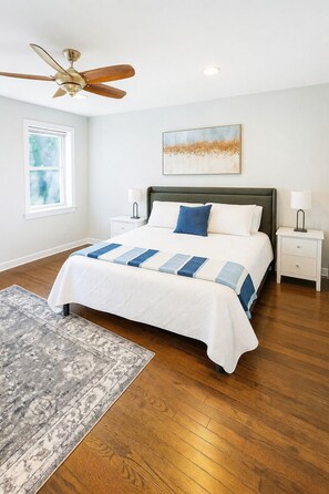 Une chambre à coucher comprenant un lit, un ventilateur de plafond, une fenêtre, une table de chevet, une lampe et un tapis.