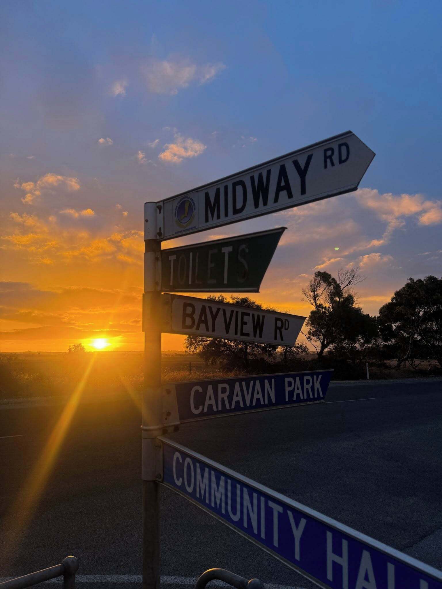 A street sign with directions to Midway Rd, Toilets, Bayview Rd, Caravan Park, and Community Hall.